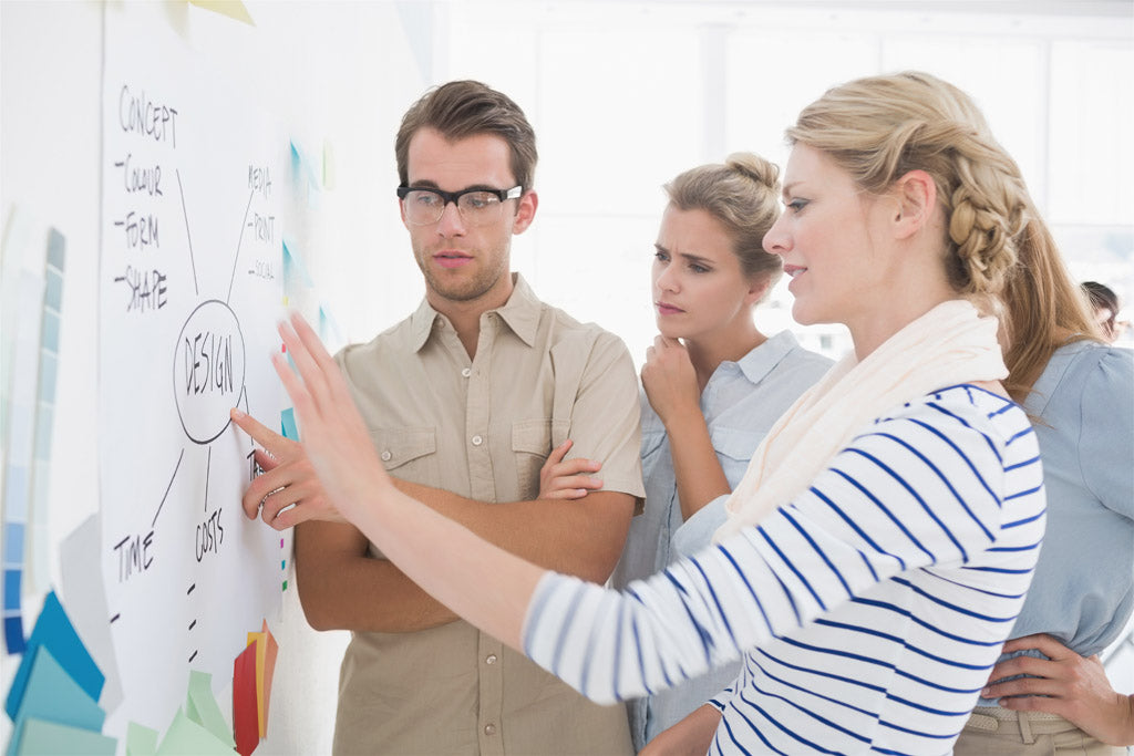 Drei Personen diskutieren ein Designkonzept an einer Wand, Markenname Master Ch integriert.