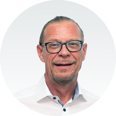 Ein Mann mit Brille und weißem Hemd lächelt vor grauem Hintergrund. Markenname: Master Ch.